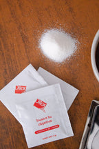 Sobres de sustituto de crema Dilox junto a taza de café